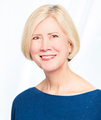 The image shows a woman with short hair wearing a blue top, posing for a portrait with a neutral background.